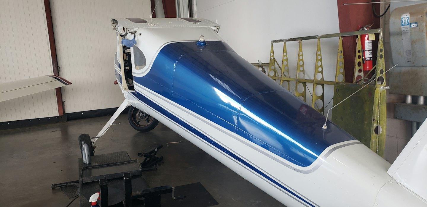 Small aircraft undergoing repair in a brightly lit hangar.
