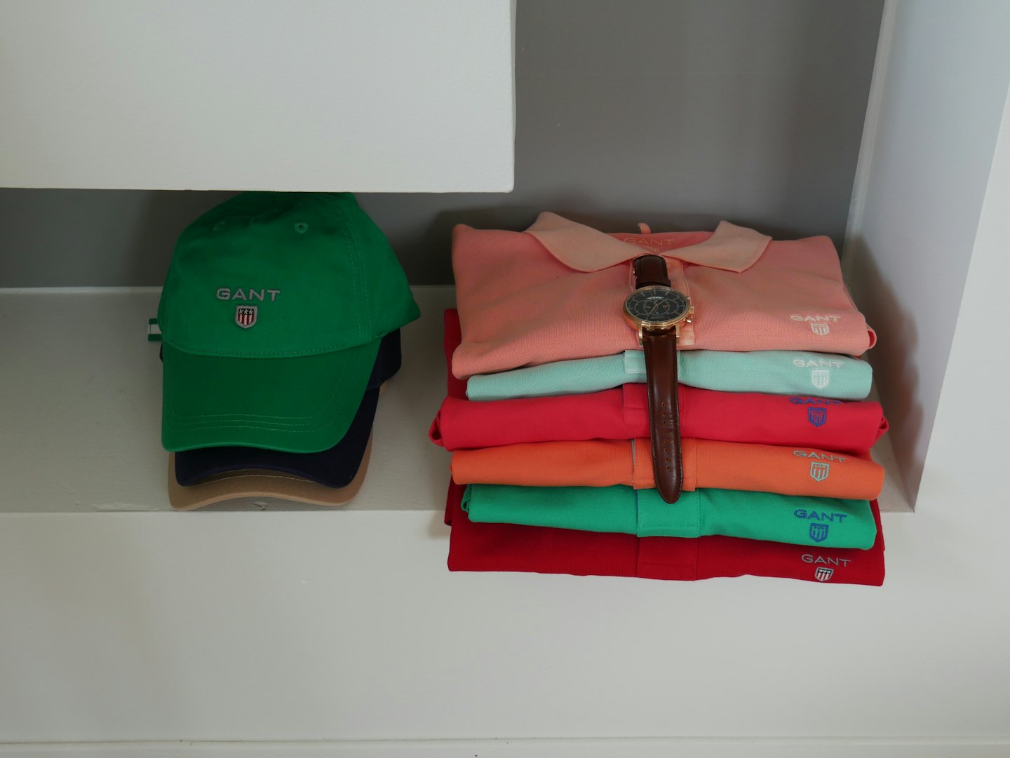 Stacked colorful polo shirts and caps with a wristwatch on display.