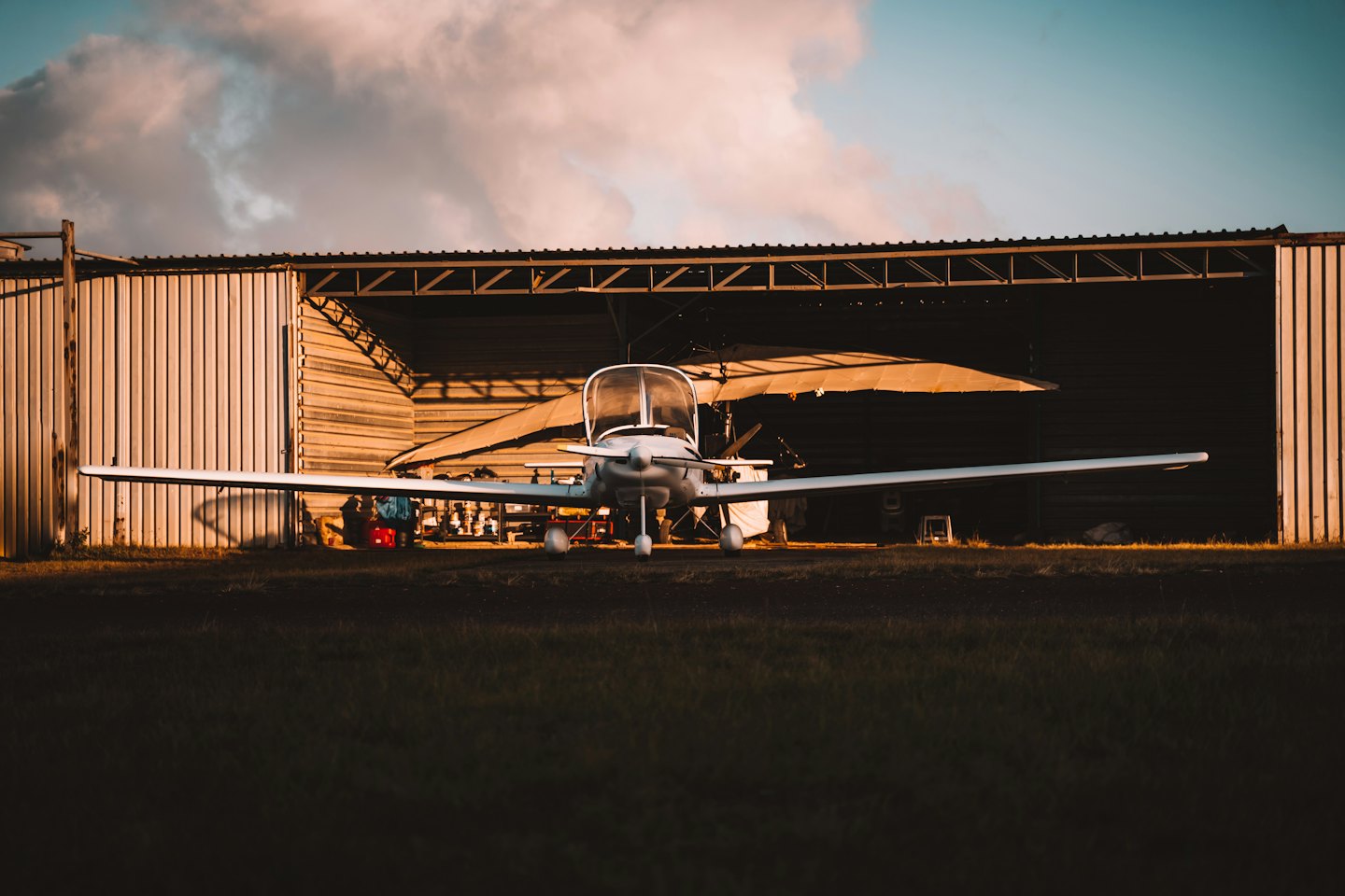 Single-engine airplane parked outside a metal hangar at sunset.