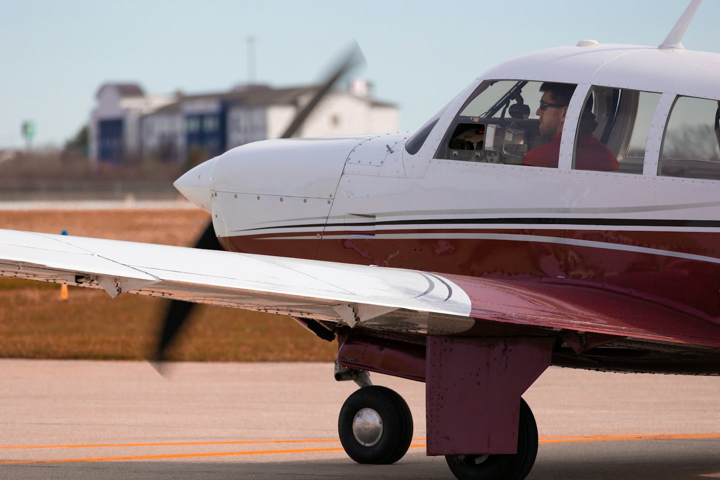 A pilot wearing sunglasses sits inside a single-engine propeller plane.